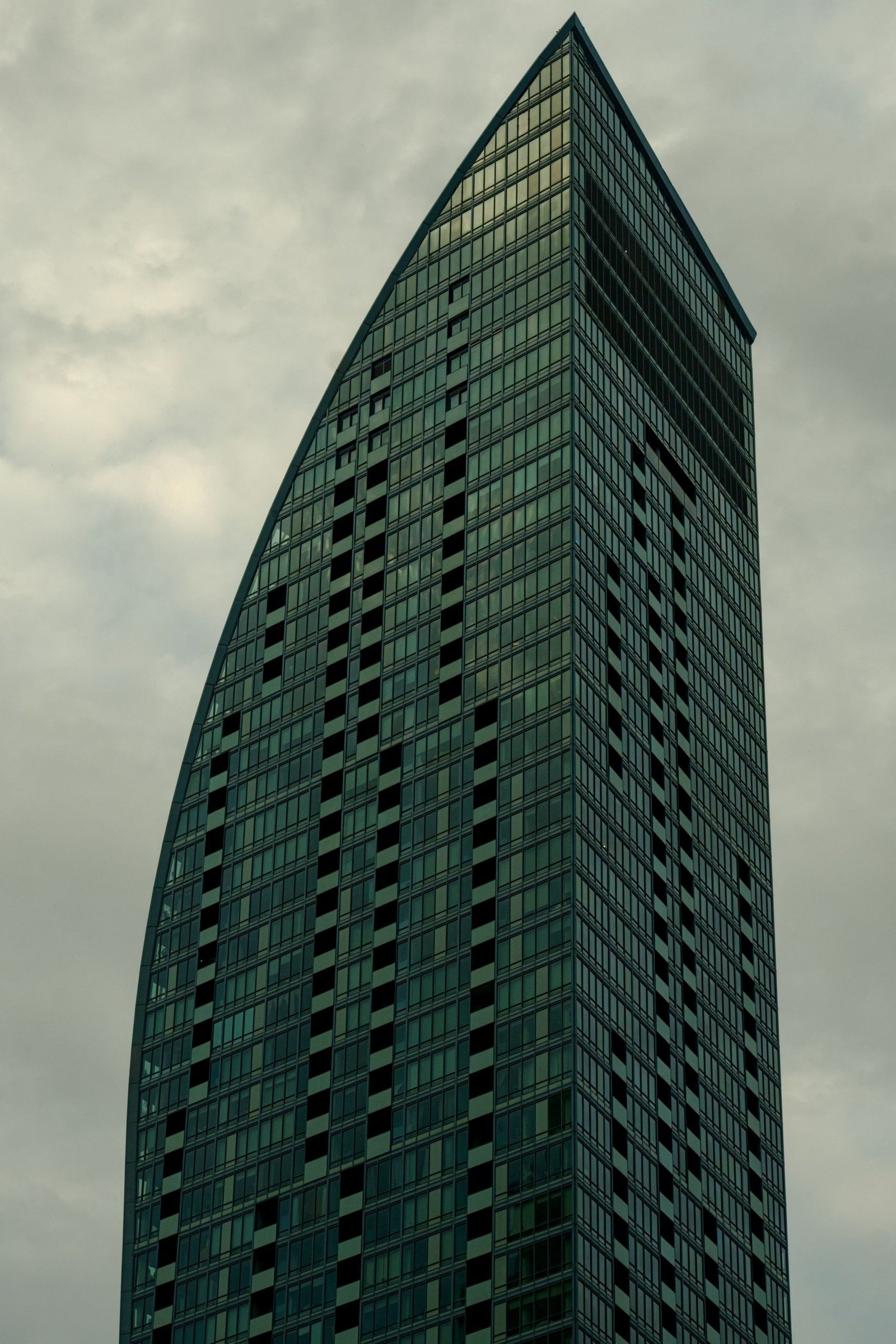 Tall, modern skyscraper in Toronto with a unique architectural design, set against grey clouds.